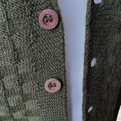 Close-up of a textured olive green knit cardigan with pink wooden buttons, worn over a white top.