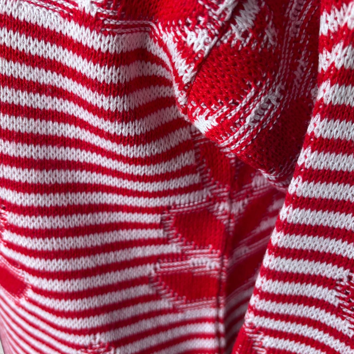 Close-up of a red and white knit fabric with horizontal stripes and a textured geometric pattern.