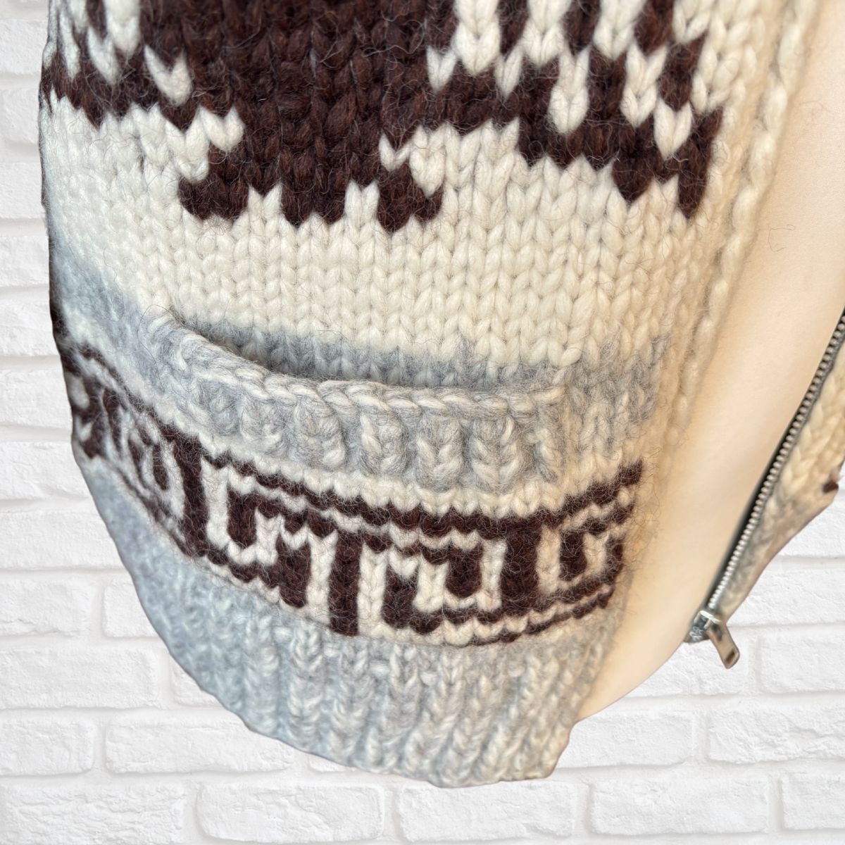 Close-up of a knitted garment’s  pocket with a pattern against a white brick wall.
