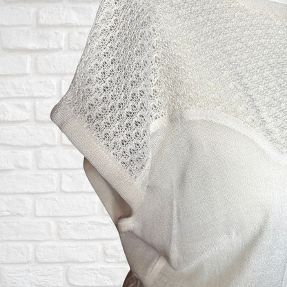 Close-up of a textured white knit dress against a white brick wall background