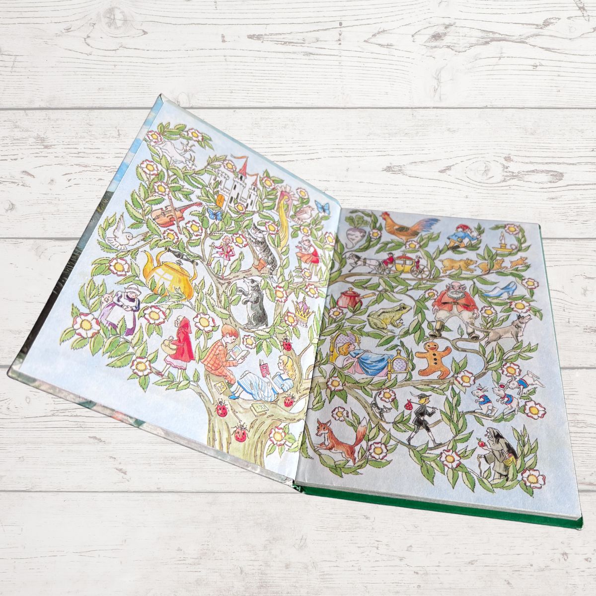An open hardcover book featuring highly detailed, colorful illustrations of cats and other animals forming a tree of life, displayed on a light-colored wooden plank surface.