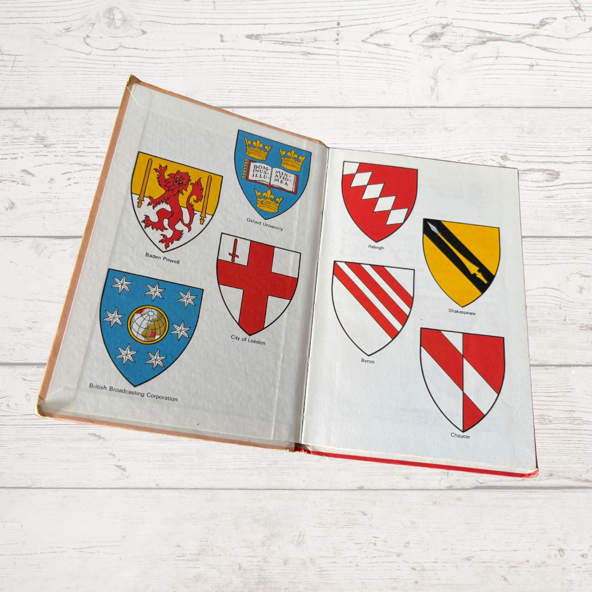Open book displaying various illustrated coats of arms on a wooden surface