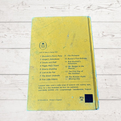A yellow Ladybird children's activity book, showing the back cover with a list of 14 activities and a small black square sticker, photographed on a white wood background.