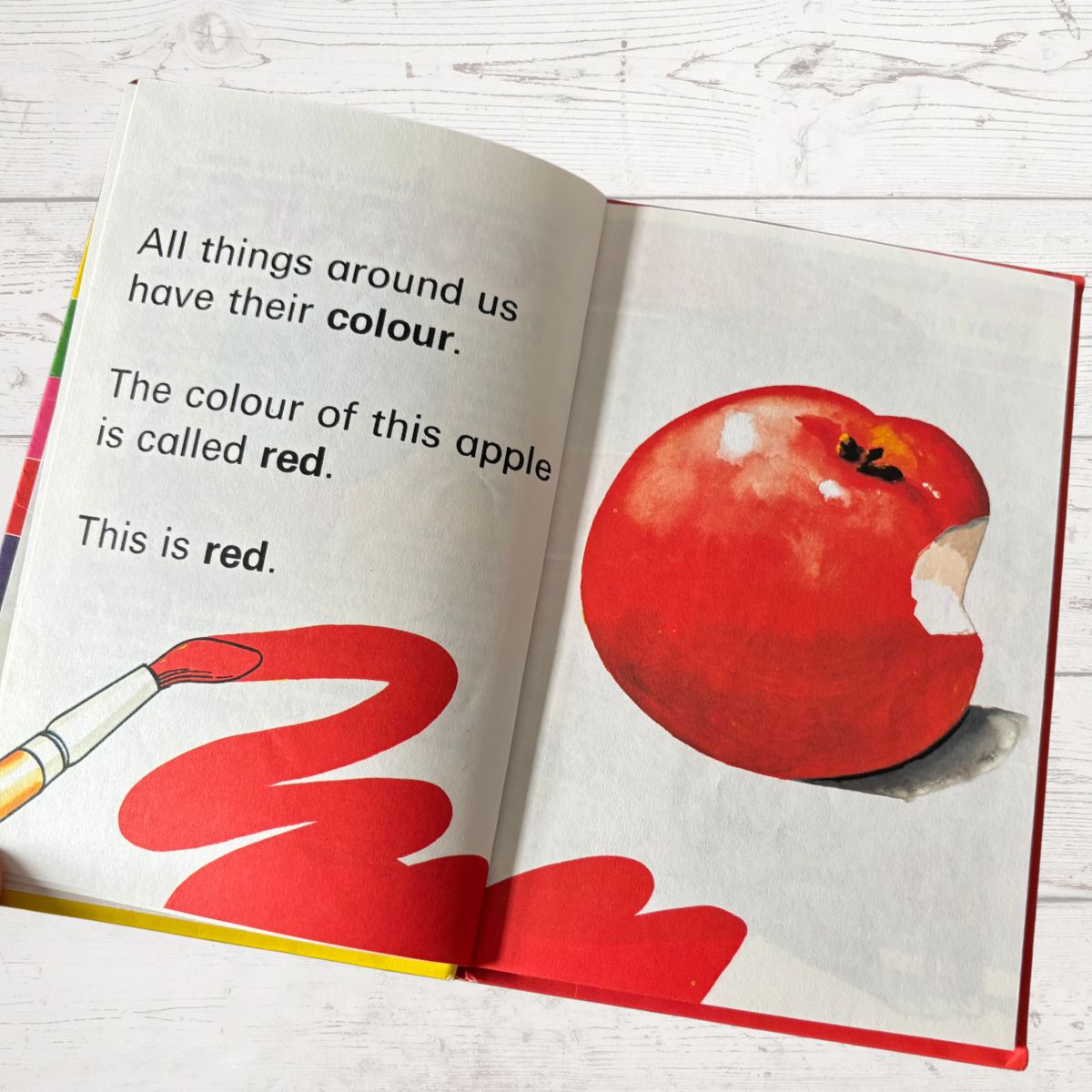 Open book with a red apple illustration and text on a white wooden surface