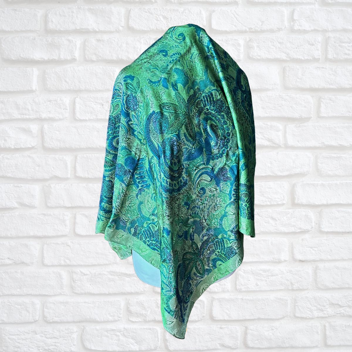 Green and blue patterned scarf draped over a white brick wall