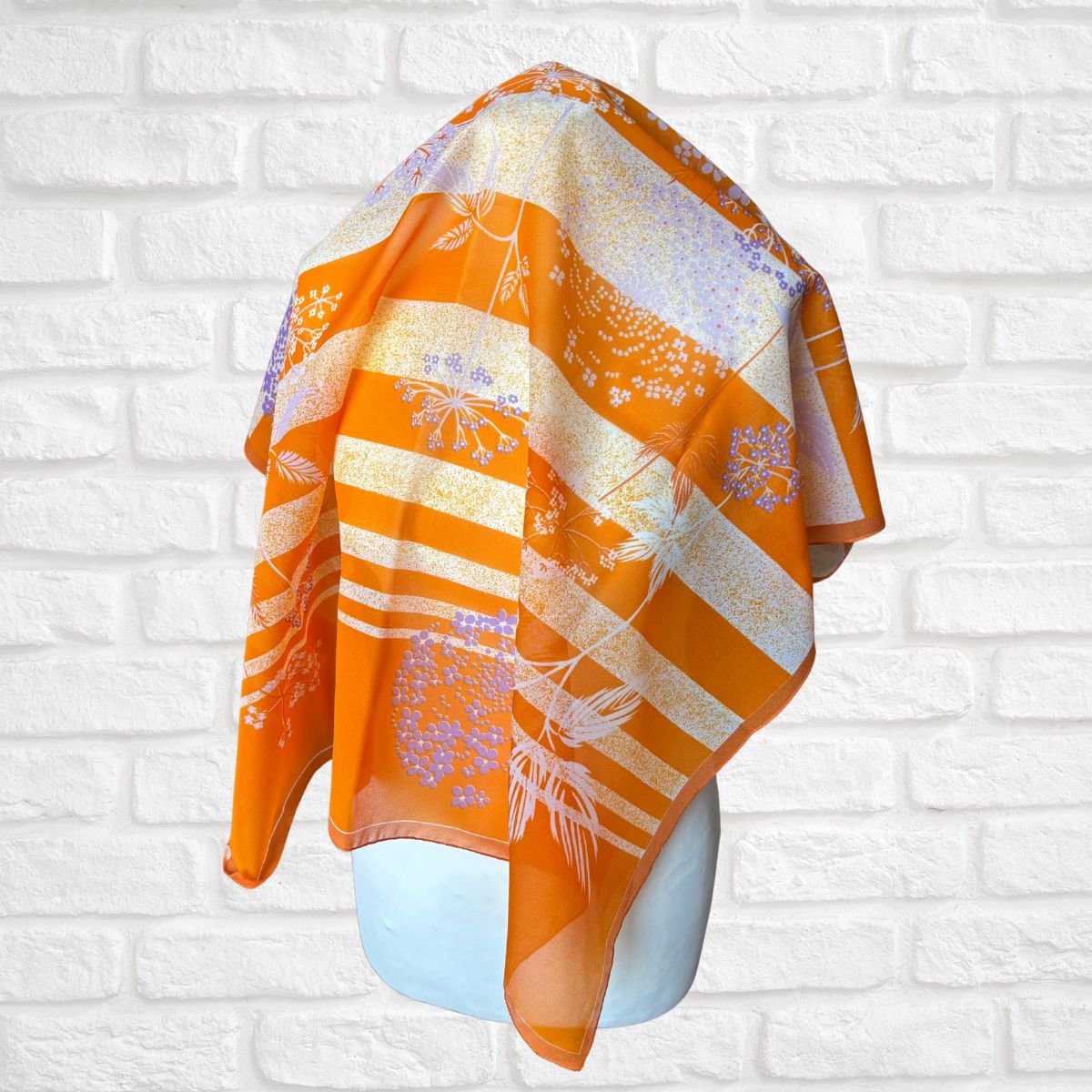Orange and white patterned scarf on a mannequin against a white brick wall.