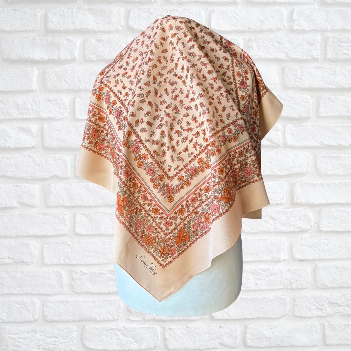 Decorative scarf with floral pattern on a mannequin against a white brick wall.