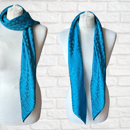 One blue scarf / 2 ways to wear on mannequins against a white brick wall.