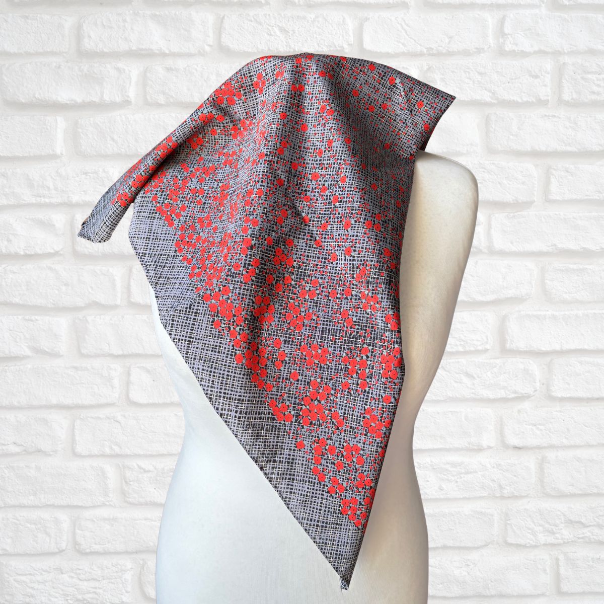 Scarf with red floral pattern draped over a mannequin against a white brick wall.