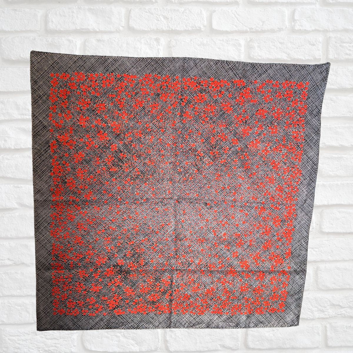 Gray scarf with red floral pattern on a white brick wall background