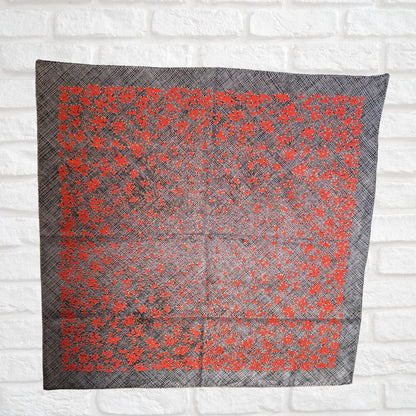 Gray scarf with red floral pattern on a white brick wall background