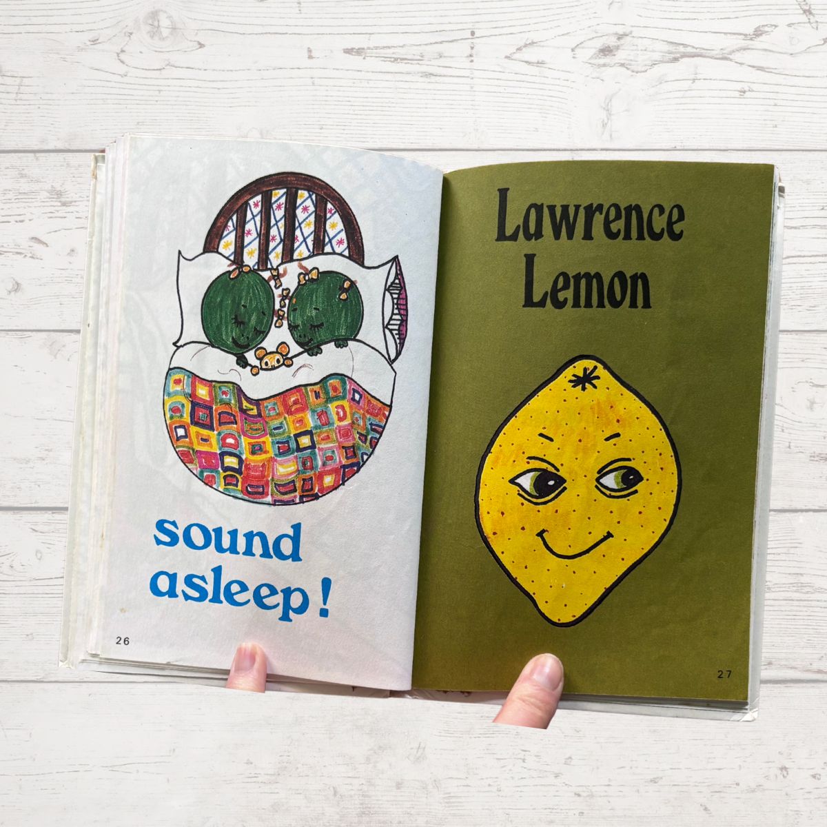 A book  open to pages with illustrations of a cat and a lemon, on a light wooden surface.