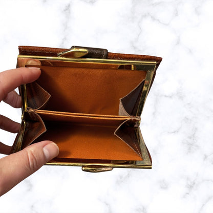 Brown leather wallet with gold frame held by a hand on a white background