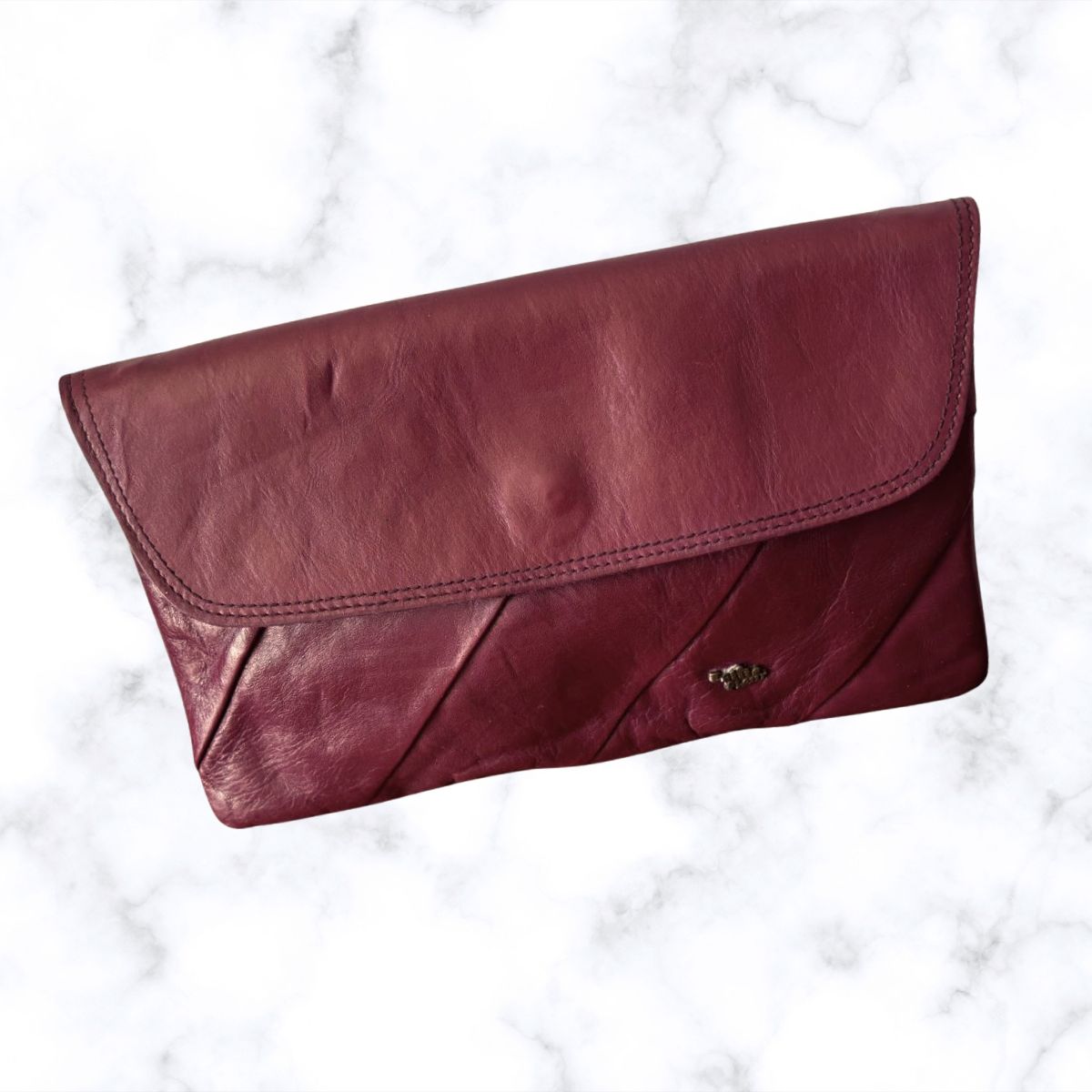 Wine coloured clutch bag on a white marble background
