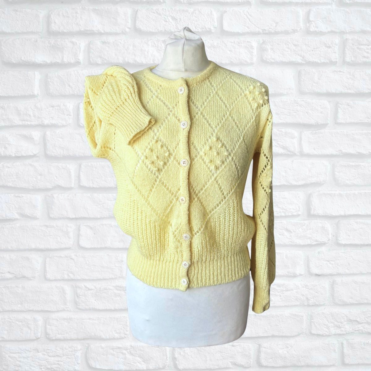 Yellow knitted cardigan on a mannequin against a white brick wall background