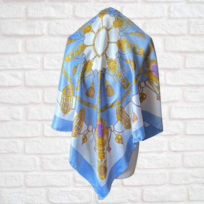Decorative scarf with gold and blue patterns on a white brick wall background