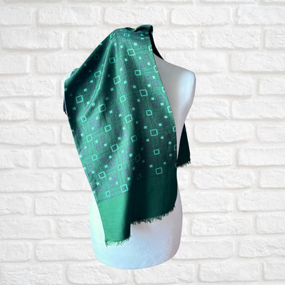 A green patterned scarf draped on a white mannequin torso, set against a white brick wall background.