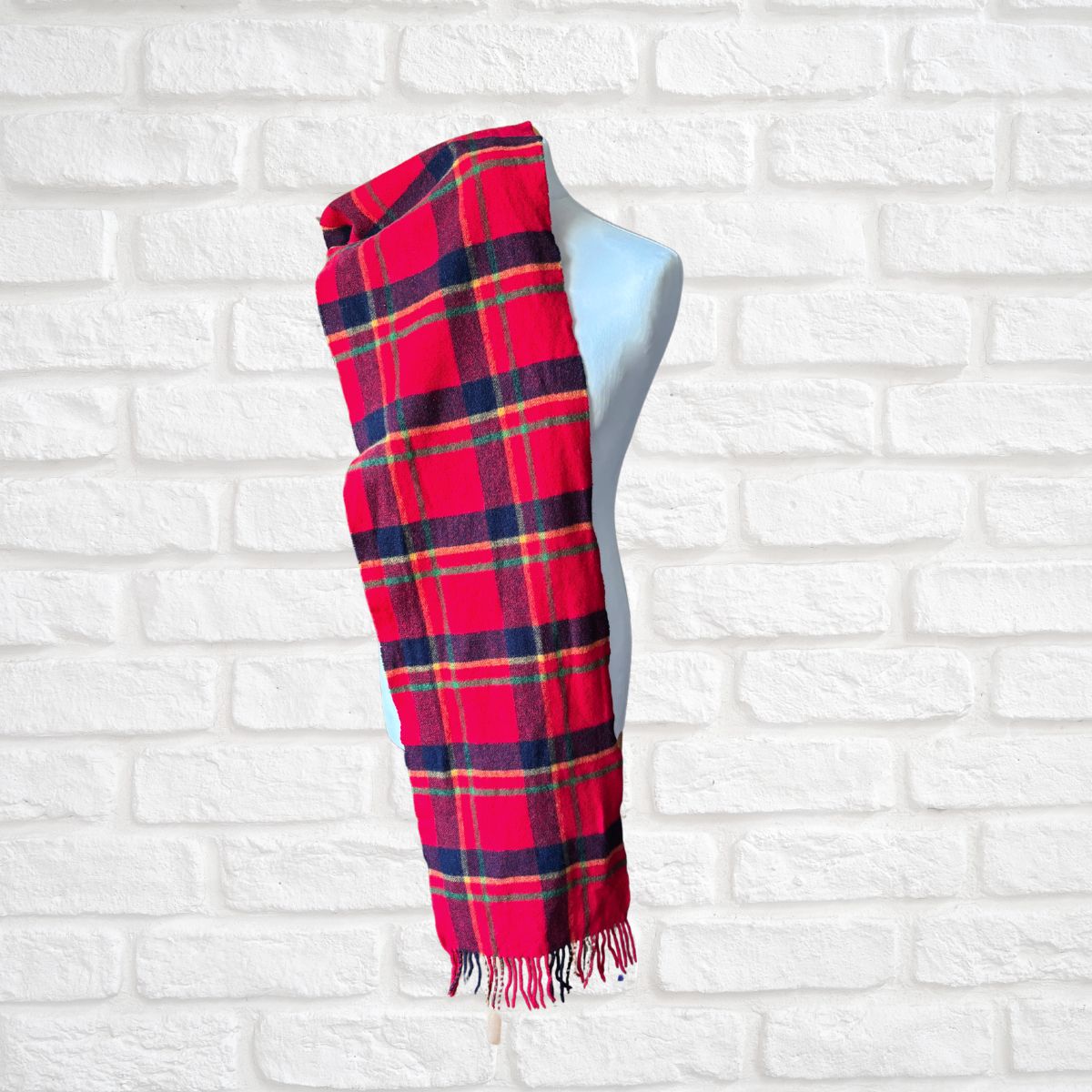 Red and blue plaid scarf on a mannequin against a white brick wall.