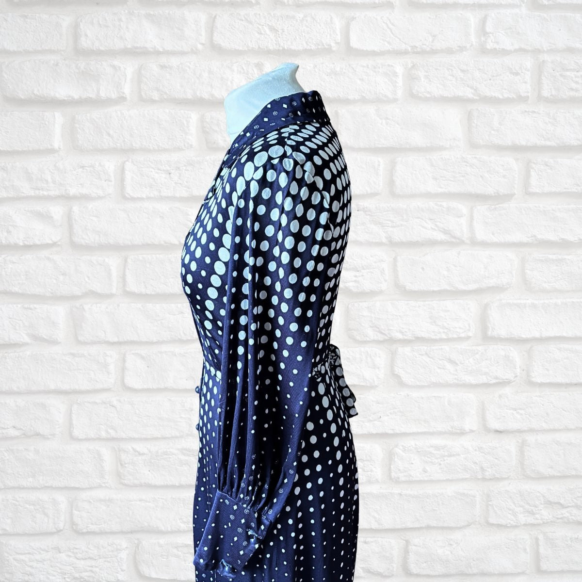 Navy blue dress with white polka dots on a mannequin against a white brick wall.