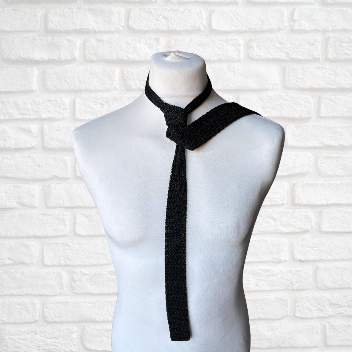 Black knitted tie on a mannequin against a white brick wall background