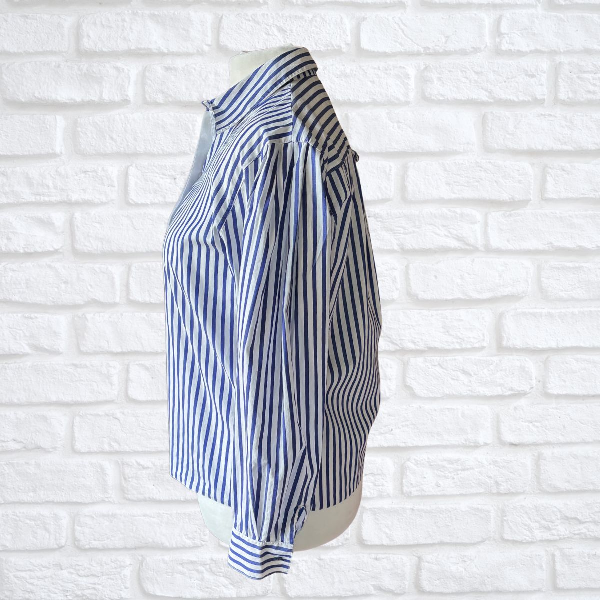 Blue and white striped shirt on a mannequin against a white brick wall background