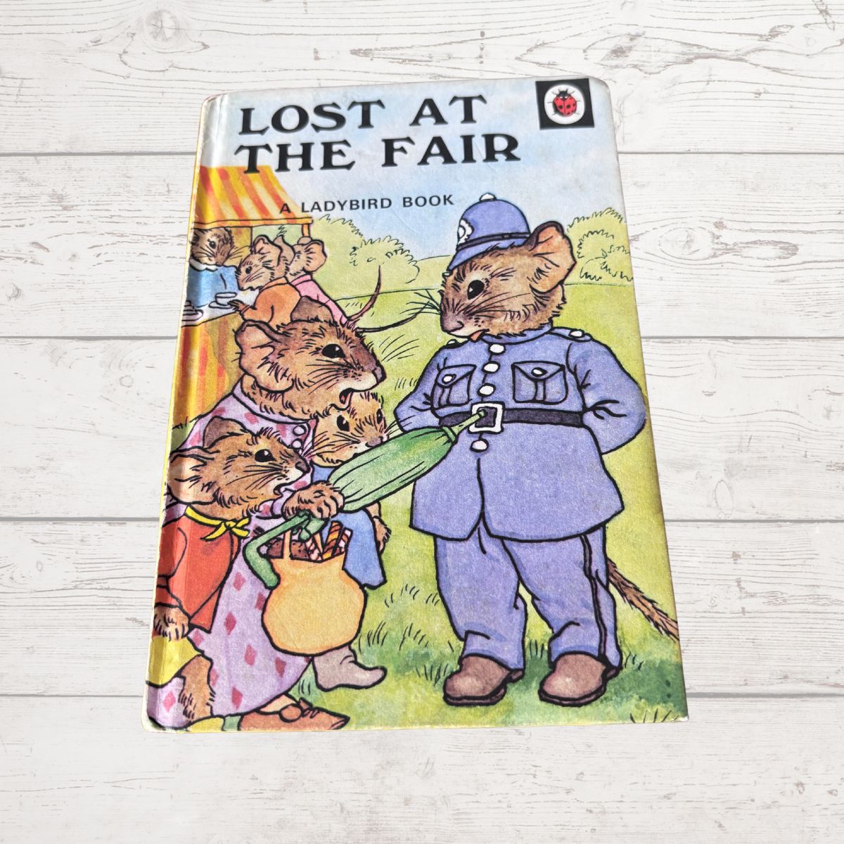 A vintage hardcover children's book titled 'Lost at the Fair' by Ladybird, featuring an illustration of mice in a fair setting, photographed on a white wooden surface.
