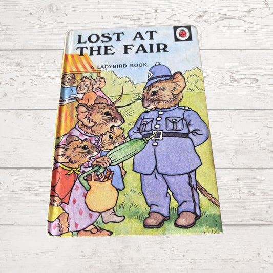 A vintage hardcover children's book titled 'Lost at the Fair' by Ladybird, featuring an illustration of mice in a fair setting, photographed on a white wooden surface.