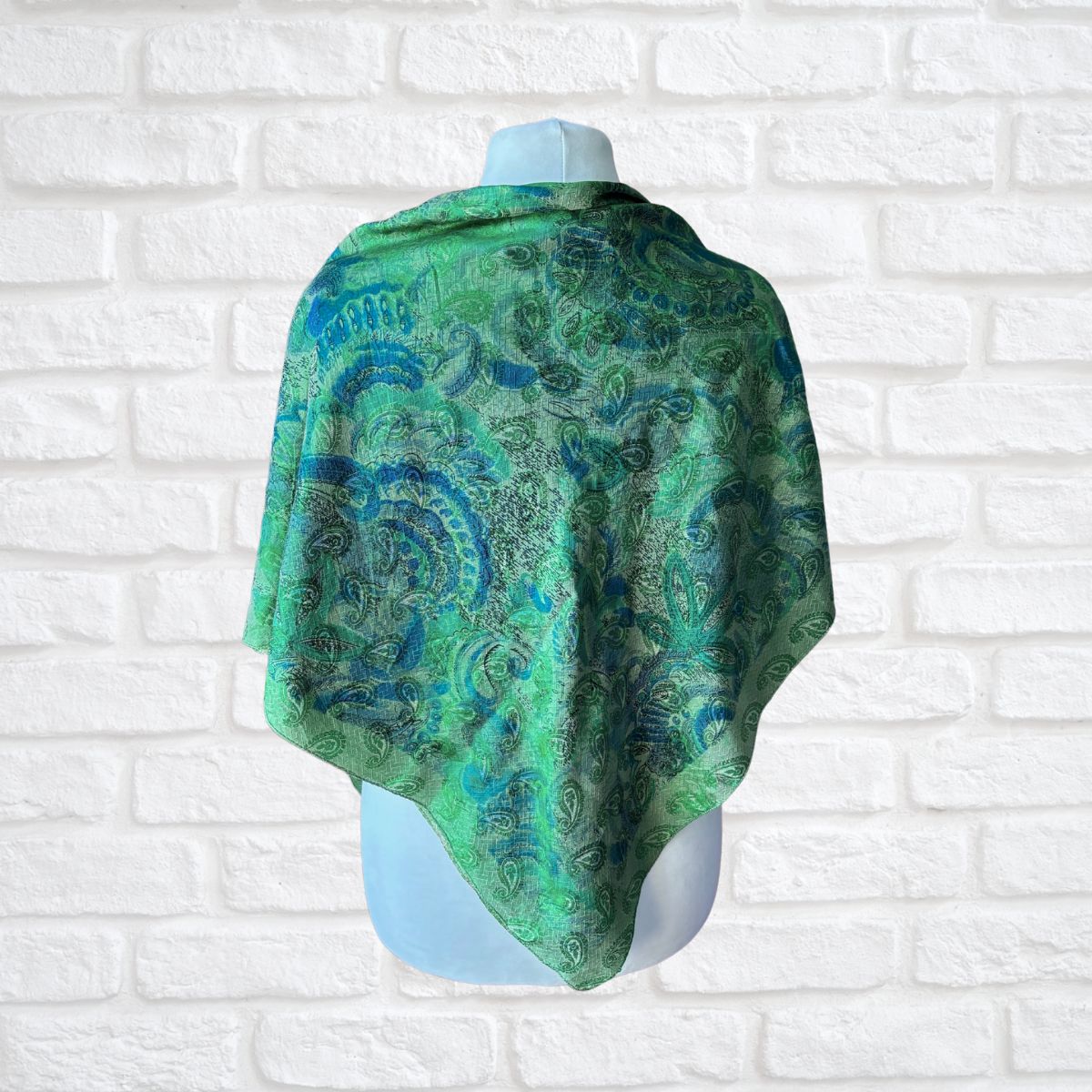 Green and blue patterned shawl on a mannequin against a white brick wall.