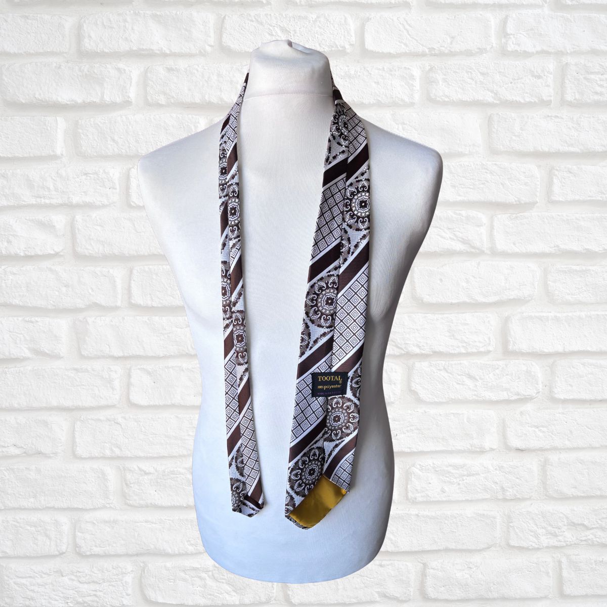 Mannequin wearing a patterned scarf against a white brick wall.