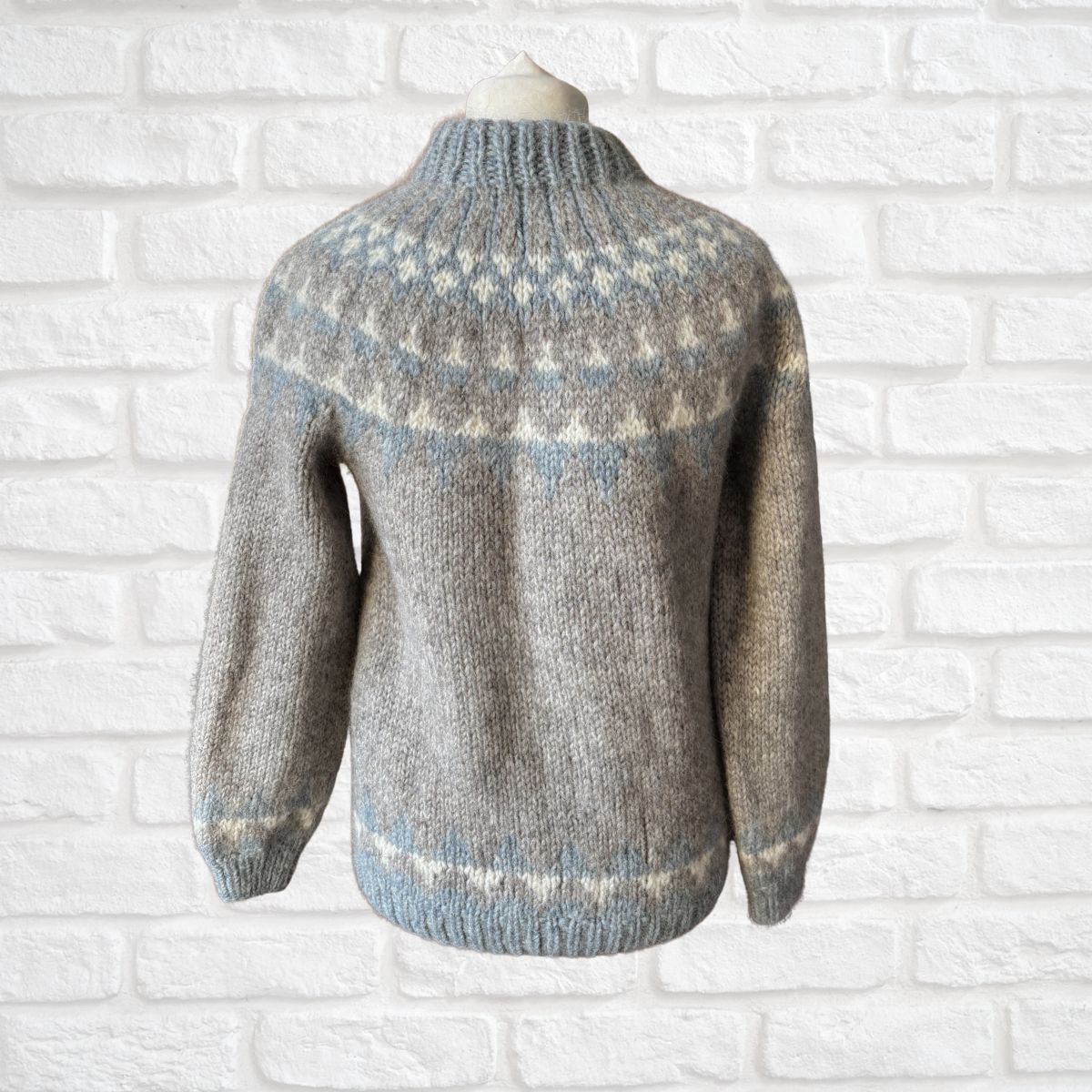 Gray knitted sweater with pattern on a white brick wall background