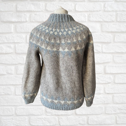 Gray knitted sweater with pattern on a white brick wall background