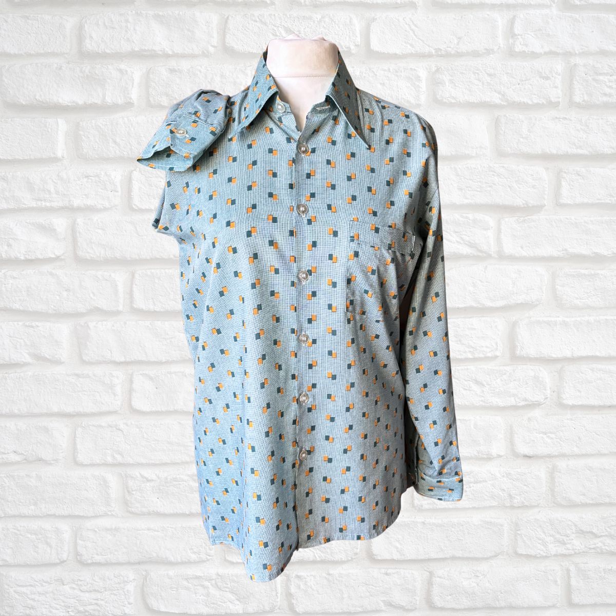 Light blue patterned mens shirt on a female mannequin against a white brick wall background