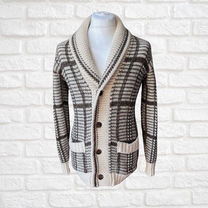A knit cardigan sweater with a shawl collar, button-front closure, and a plaid pattern, displayed on a white mannequin torso against a white brick wall background.