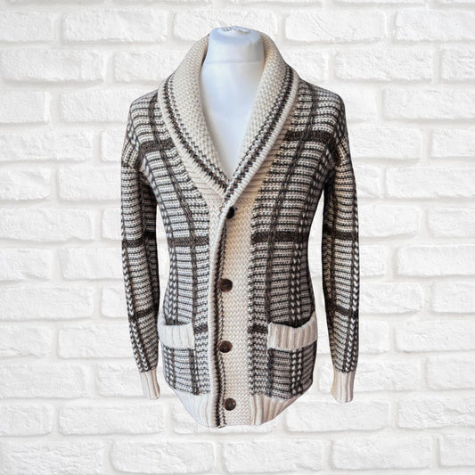 A knit cardigan sweater with a shawl collar, button-front closure, and a plaid pattern, displayed on a white mannequin torso against a white brick wall background.