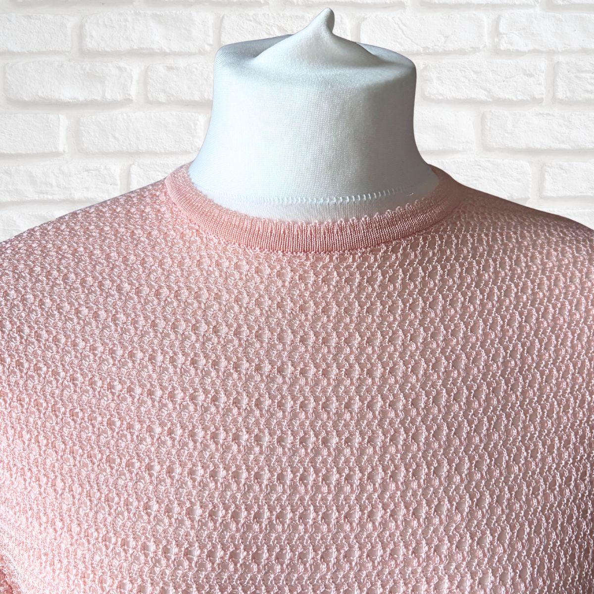 A light pink textured knit dress displayed on a white mannequin torso against a white brick wall background.