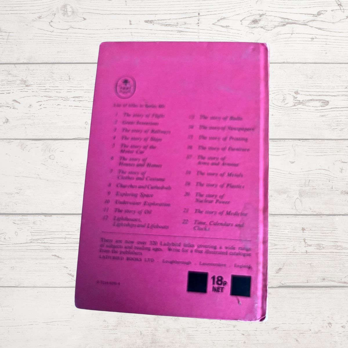 A pink book cover with printed track listings and an 18-net price box, photographed on a whitewashed wood surface.