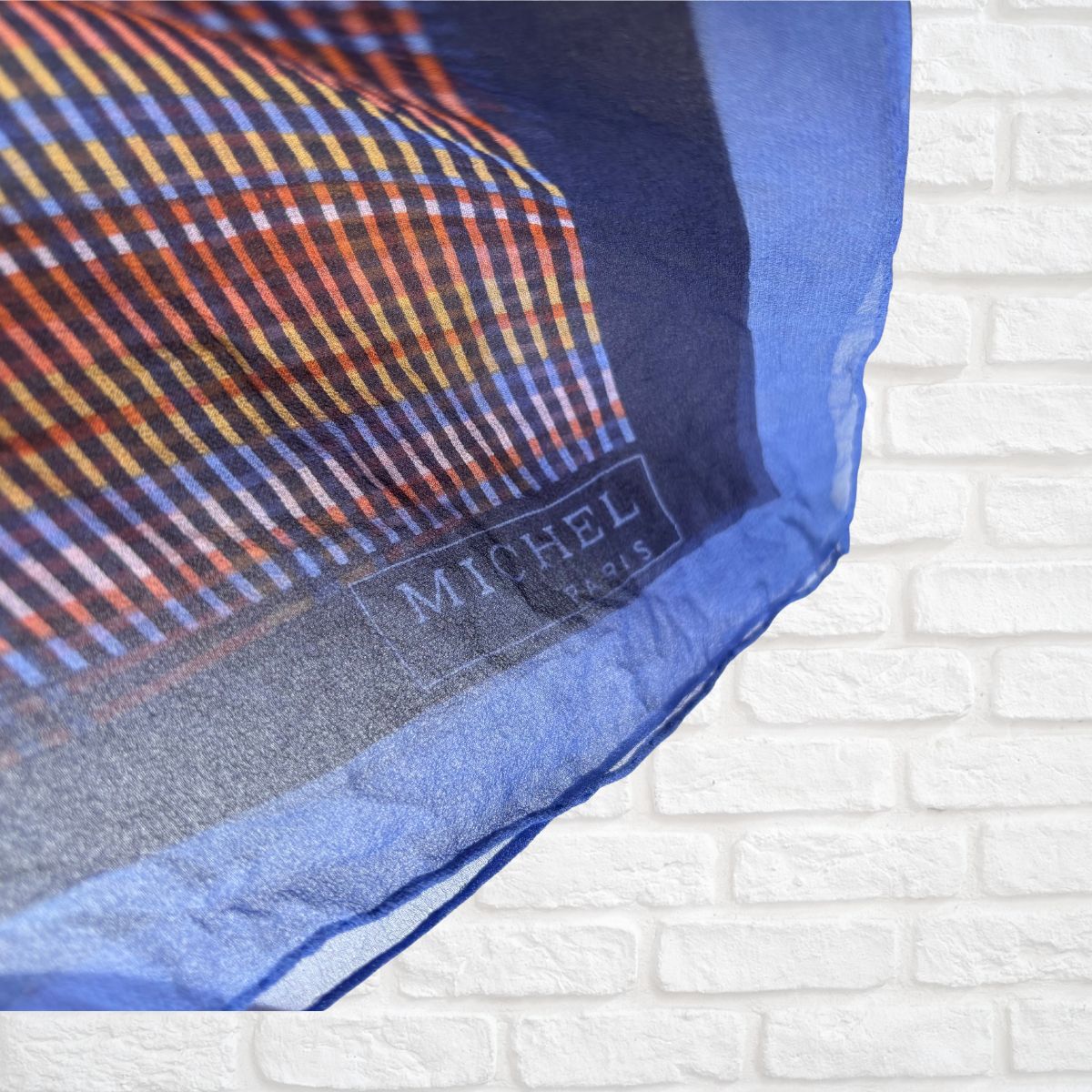 Scarf with a visible Michel Paris brand label on a white brick background