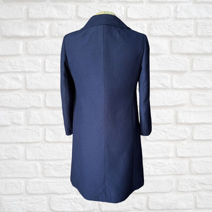 A navy blue longline blazer or coat displayed on a mannequin torso, shown from the back against a white painted brick wall.