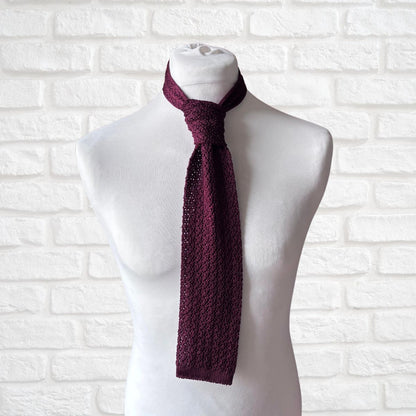 Mannequin wearing a burgundy knitted scarf against a white brick wall.