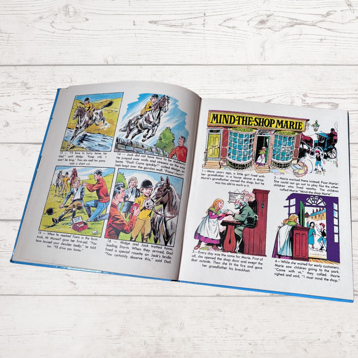 An open vintage-style illustrated book spread laid flat on a white wood surface. The pages contain multiple cartoon panels and printed text, including a prominent title reading 'MIND THE SHOP MARIE.