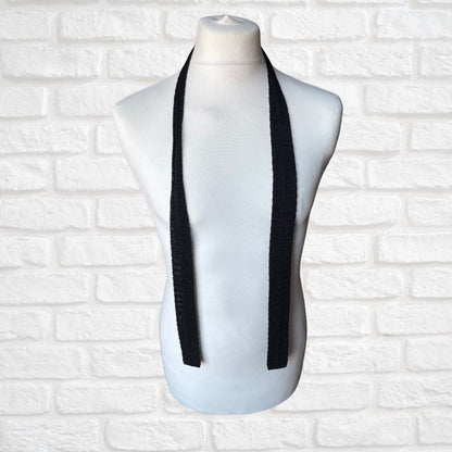Black 60s skinny tie on a mannequin bust against a white brick wall background