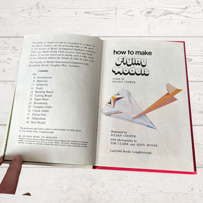 Open book titled 'How to Make Flying Models' with illustrations on a wooden surface