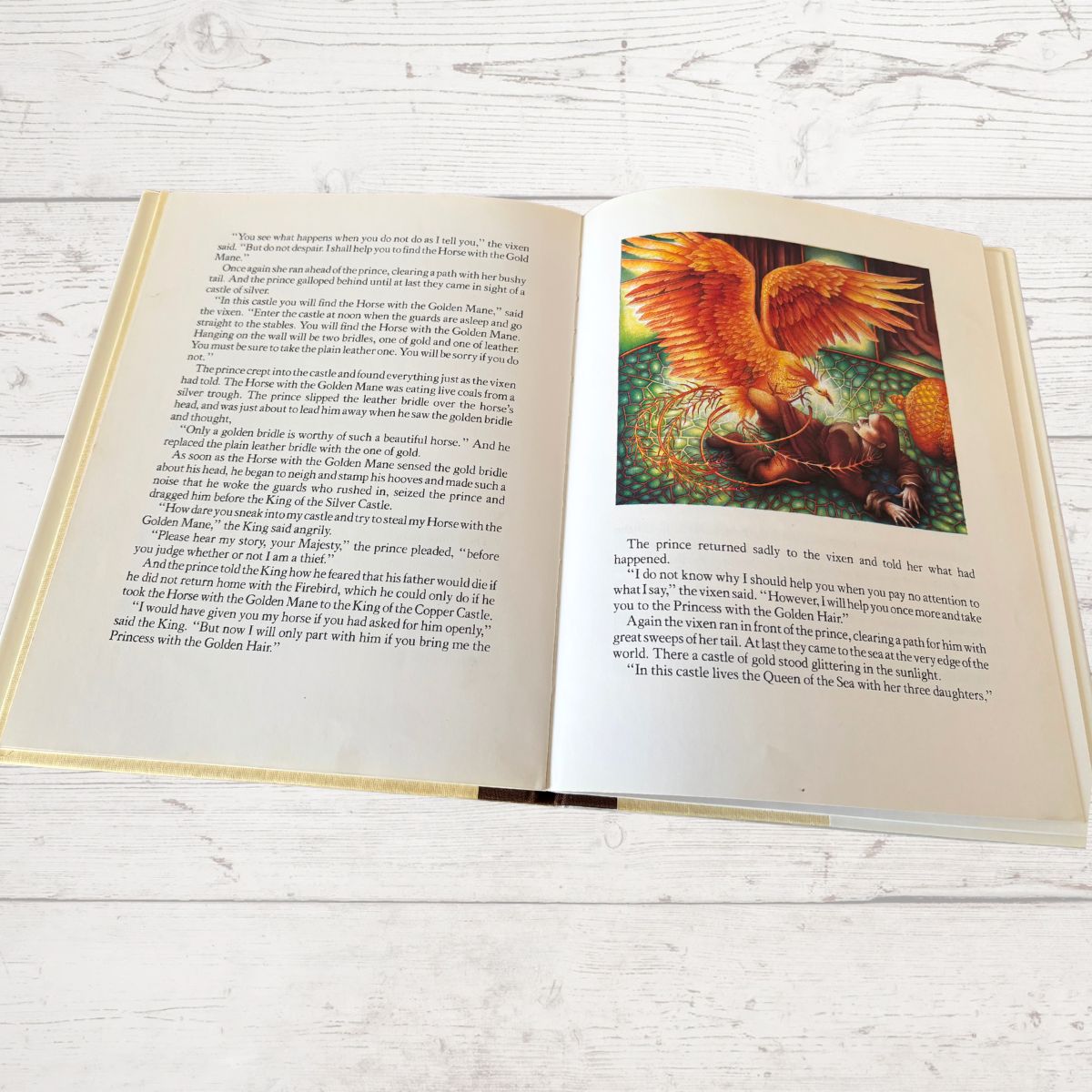 An open children's picture book lying on a light whitewashed wooden surface. The left page has printed text, and the right page shows a colorful illustration of a golden horse with a rider.