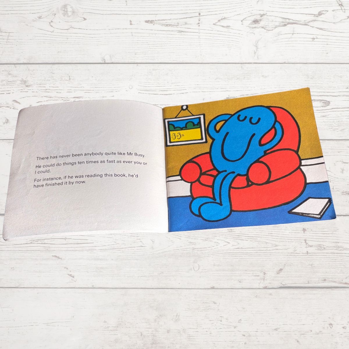 Open book with a colorful illustration of a blue creature on a yellow background, placed on a wooden surface.