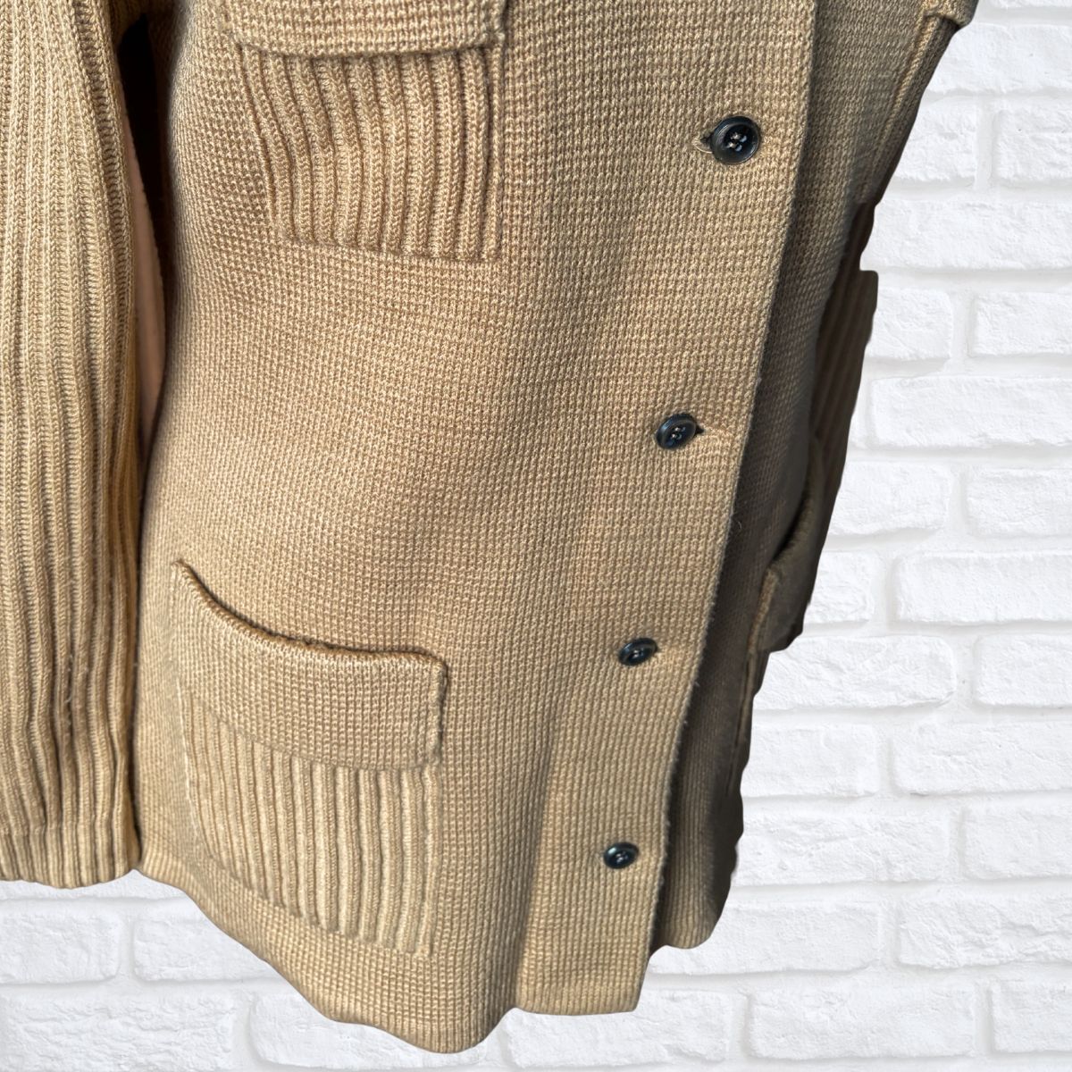 Tan  knitted cardigan with brown  buttons on a white brick wall background