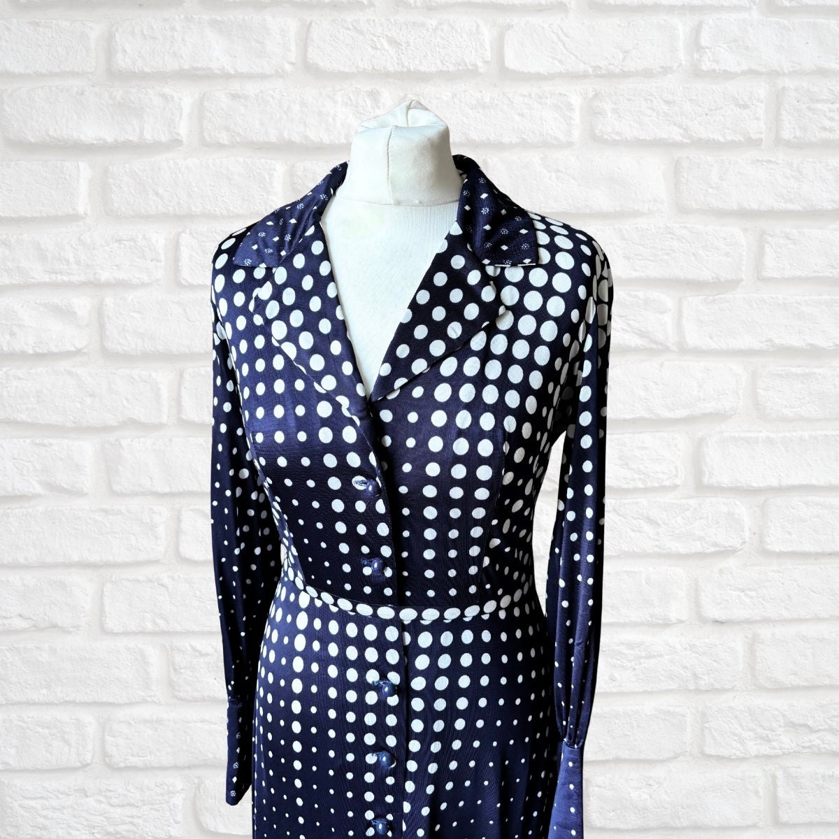 Navy blue dress with white polka dots on a mannequin against a white brick wall.