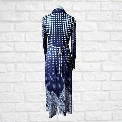 Navy blue dress with white polka dot pattern on a mannequin against a white brick wall.