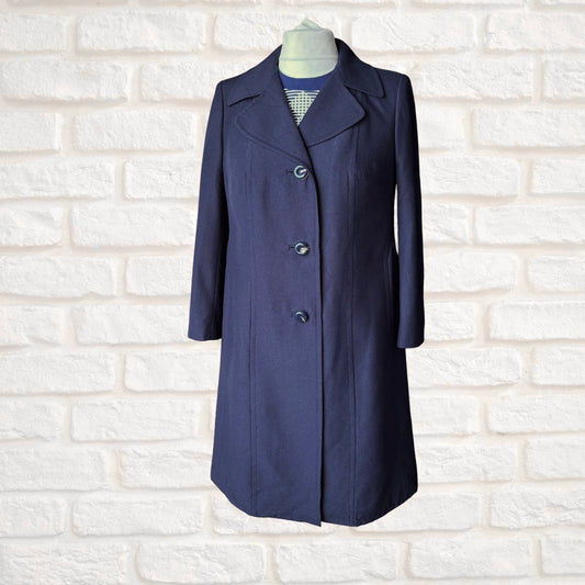A navy blue knee-length coat with notched lapels and three front buttons, displayed on a mannequin torso against a white brick wall background.