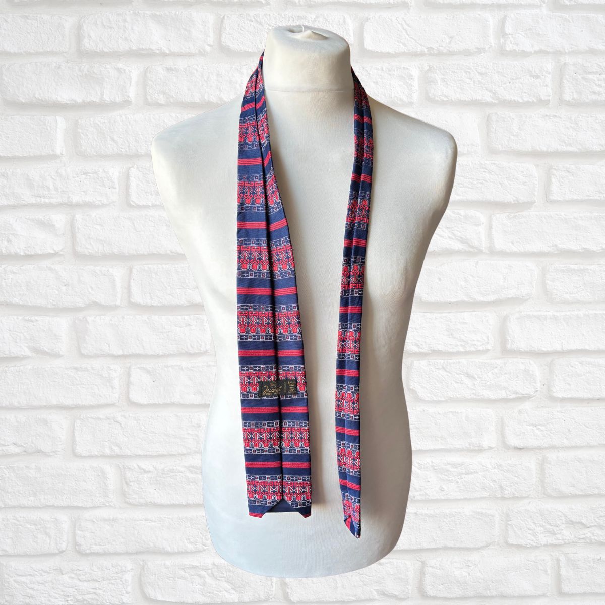 Mannequin wearing a blue and red patterned tie  against a white brick wall.