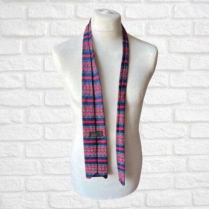 Mannequin wearing a blue and red patterned tie  against a white brick wall.